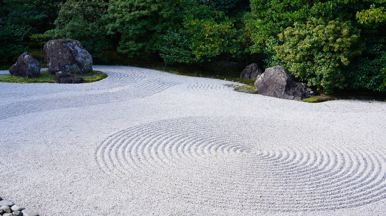 A beautifully raked Zen garden enclosed by tall hedging plants