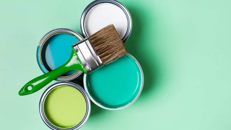 Four paint cans with various paint colors are arranged on a green background with a paint brush on top