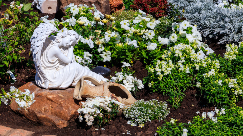 A small decorative statue in a garden surrounded by plants