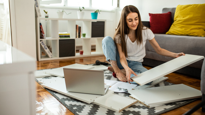 A woman assembles a piece of furniture on her floor