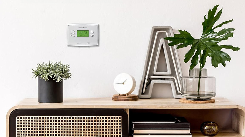 A Honeywell programmable thermostat sits above a shelf with decorative items on it