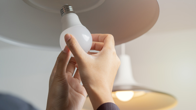 Two hands are shown installing a traditional LED lightbulb