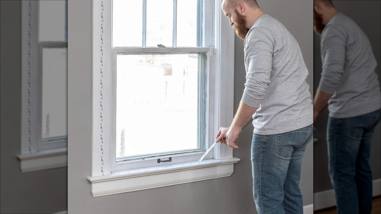 A man applies double-sided tape to a window frame