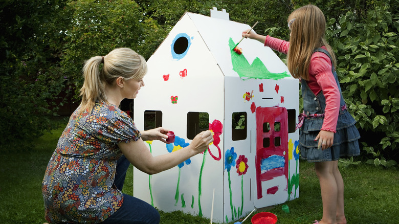 Mother and child painting cardboard house outside