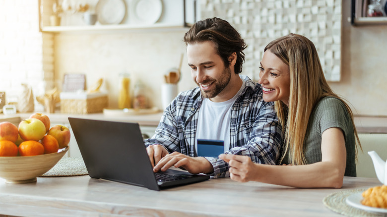 smiling young couple browsing laptop at kitchen table