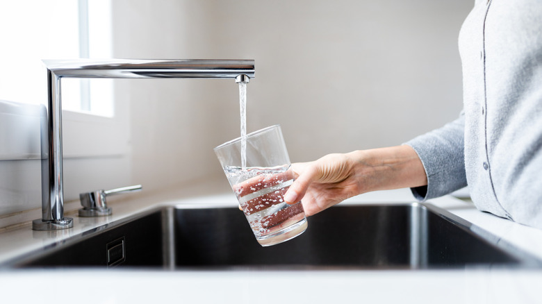 A person filling a glass with water at the sink