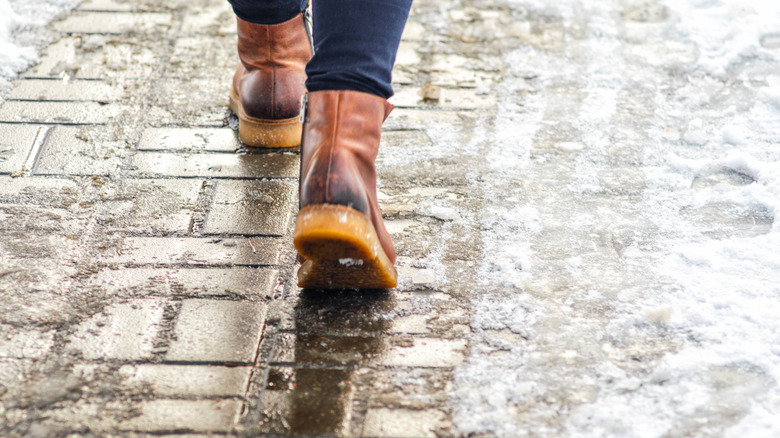 person wearing brown snow boots walking on sidewalk with melted ice