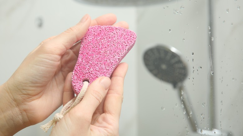 Hands hold up pink pumice stone in shower