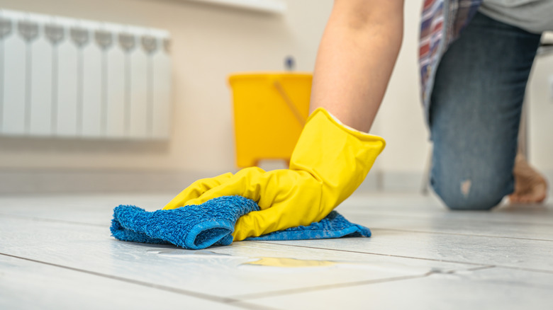 Woman cleaning stone tile floors using a blue microfiber cloth and gloves