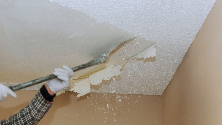 A person using a tool to scrape off a popcorn ceiling