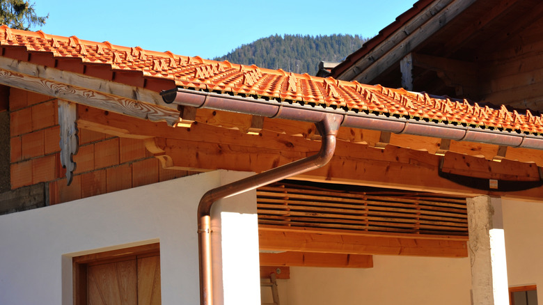 copper rain gutter in home with white walls and orange roof