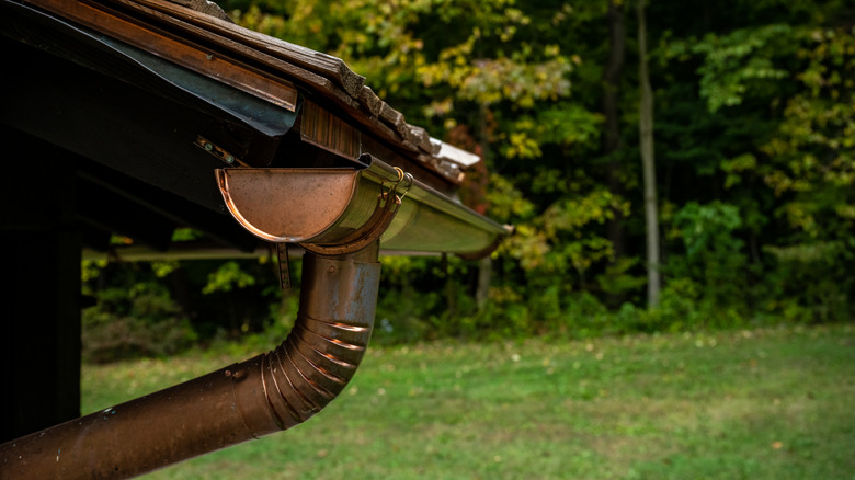 copper gutter on roof of home with green woods in the background