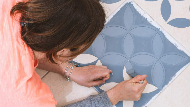 A woman painting floor tiles by hand with a stencil