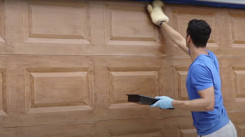 A man applying paint to create a faux wood effect on a garage door