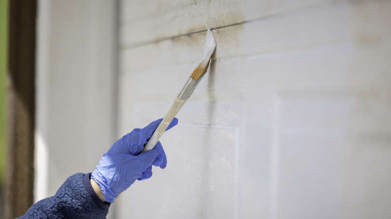 A gloved hand seen applying white primer to garage door