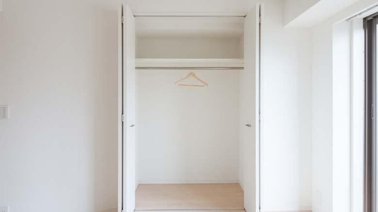 room with empty closet with white open doors and one hanger on the closet rod