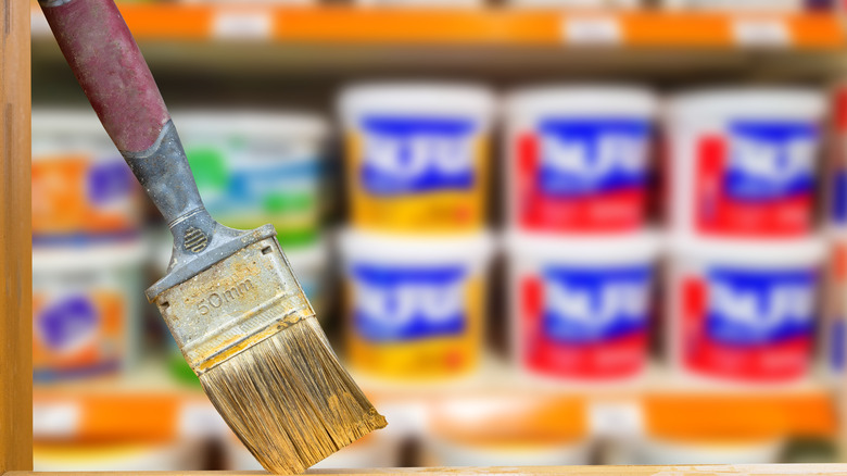 Paintbrush leaning against wall with cans of paint in the background