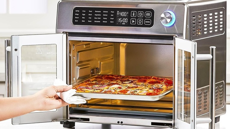 A person pulling a pizza out of an Emeril Lagasse French Door Air Fryer 360