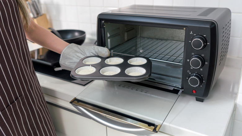 A person putting a muffin tin in a countertop oven