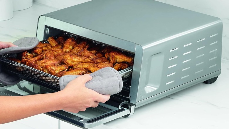 A person pulling a tray of chicken wings out of a Ninja Flip oven