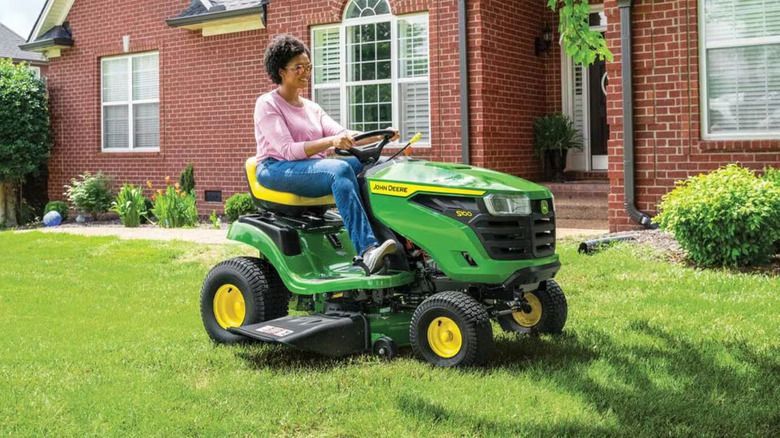 A person driving a John Deere S100 riding lawn mower