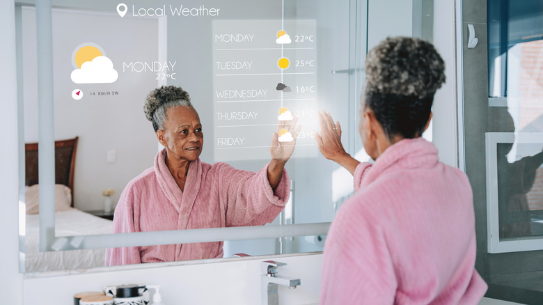 Woman in pink robe checking weather on smart mirror