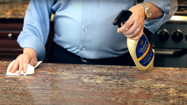 A man sprays a magma gold granite countertop with cleaner.