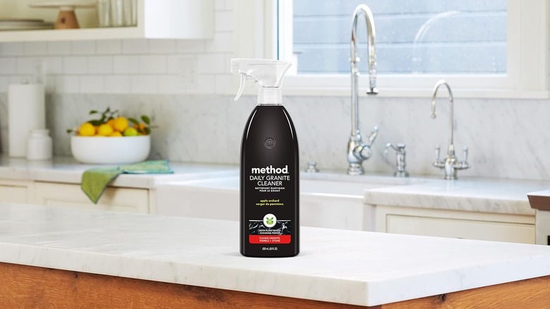 A granite cleaner spray bottle sits on white granite kitchen counters.