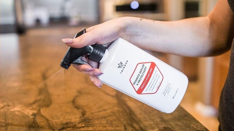 A woman sprays brown veined granite with sealer disinfectant.