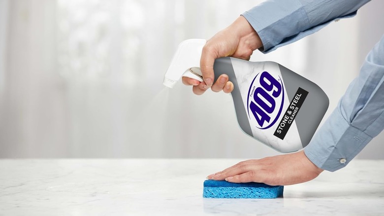 A person using cleaner with a blue sponge on a countertop.