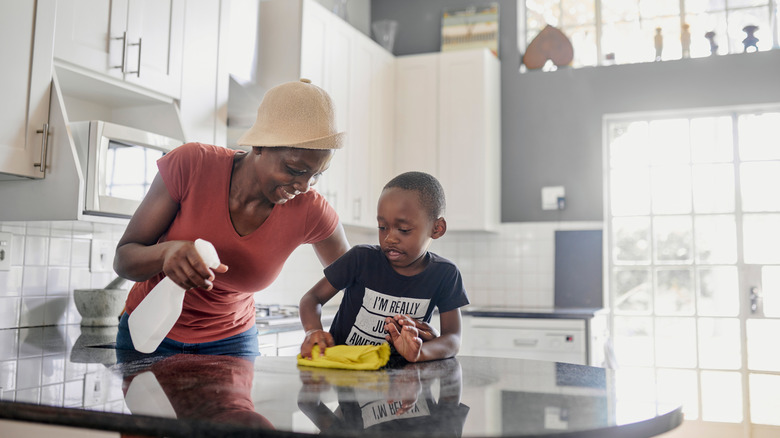 A woman and boy clean a granite countertop in the kitchen.