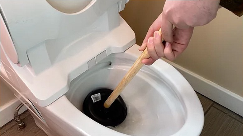 hands unclogging toilet with plunger