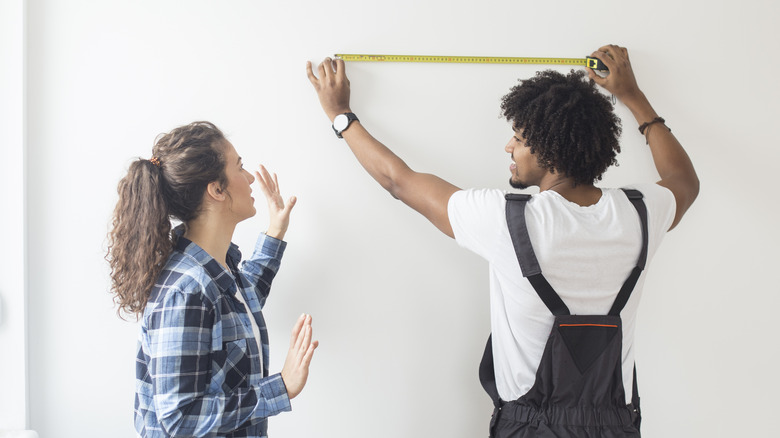 couple using tape measure on wall