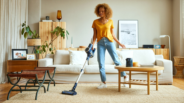 Young woman vacuums living room carpet with cordless vacuum