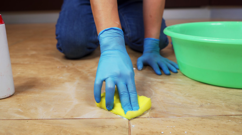 Gloved hands scrubbing marble grout with a sponge