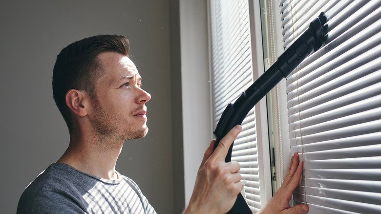 Man vacuuming window blinds