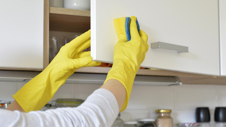 Individual wearing cleaning gloves and using a sponge to clean cabinets