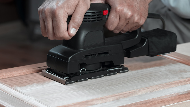 Person sanding a cabinet door.