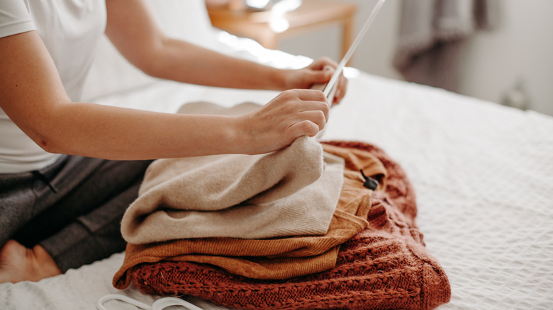 Woman folding sweater on bed