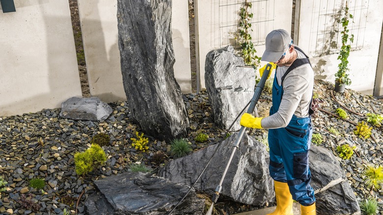 A man sprays gravel in a yard