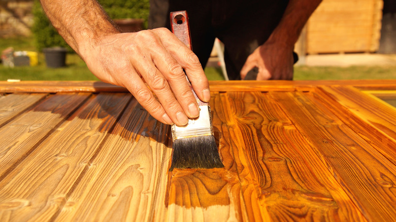 Person varnishing wood door outside