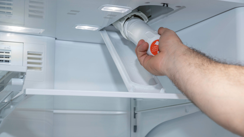 A man's arm installing a water filter in a fridge.