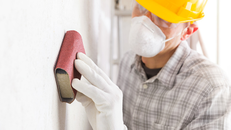 Man scraping wall with sandpaper