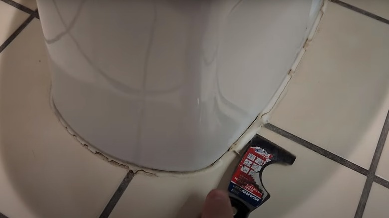 person removing caulk from toilet base