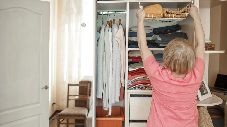 Older woman stores clothing in a tall well-organized closet