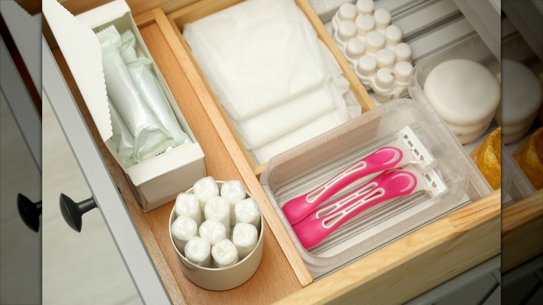 A neatly organized bathroom drawer holds pink razors and other personal care items