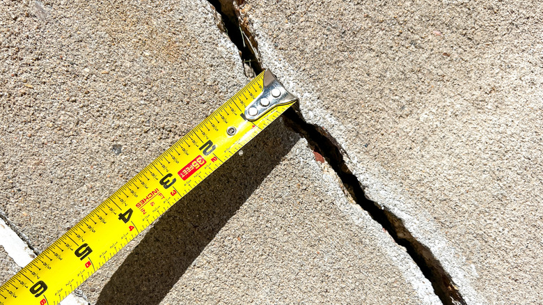 Large crack in a concrete driveway measured with a tape measure