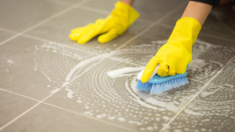 Person wearing yellow gloves scrubbing tile flooring