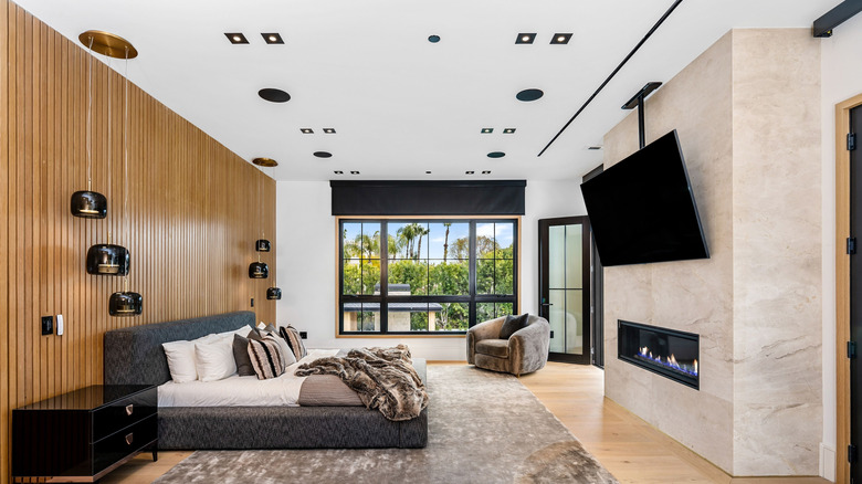 Bedrooom with wood accent wall, lighting fixtures, television, bed, fireplace, couch and a large window