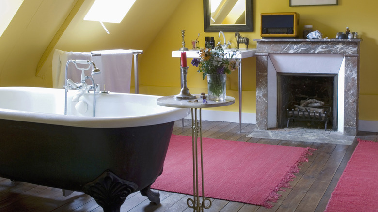 A fireplace in a bathroom with red rugs and a black claw foot tub